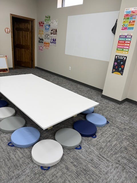 Classroom with a low white table and round floor cushions on carpet