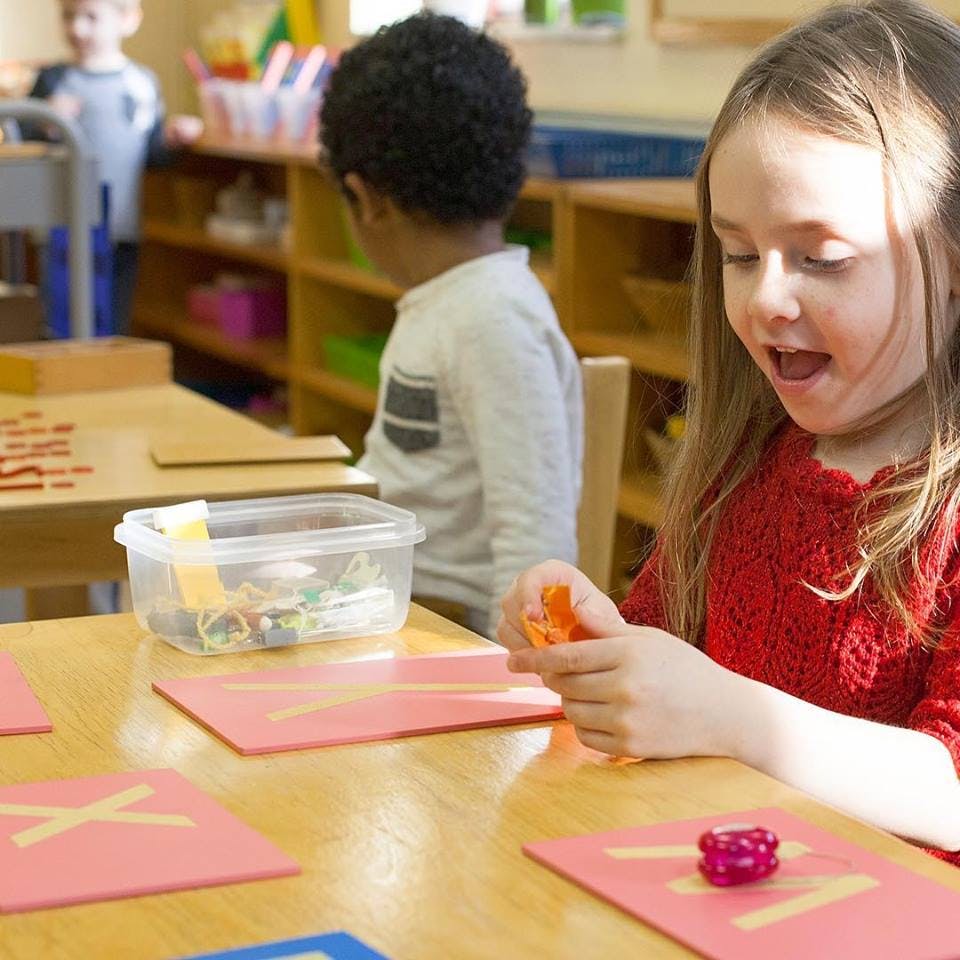 Child playing with an orange toy at a table in a classroom