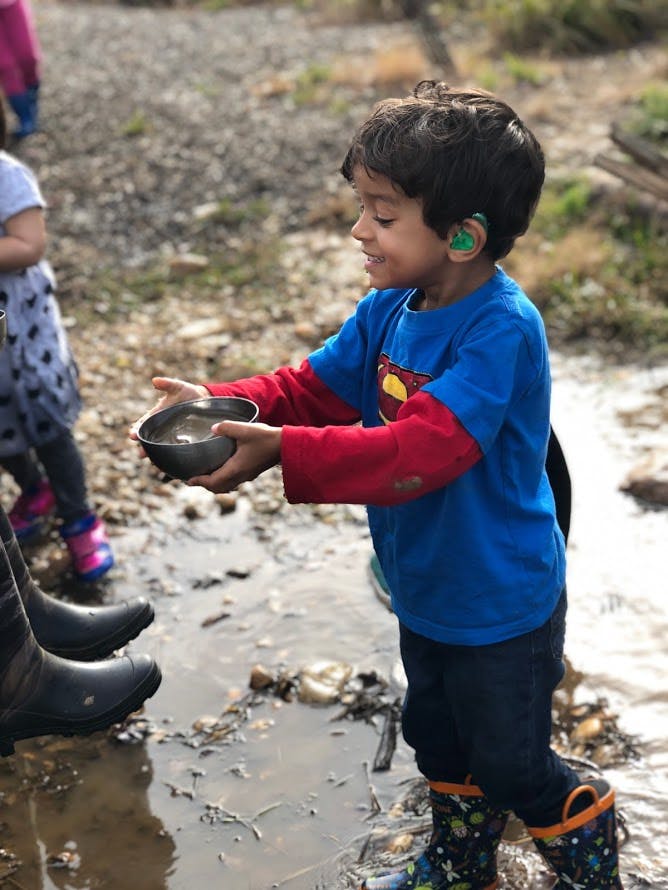 Child holding a bowl of muddy water while standing in a puddle