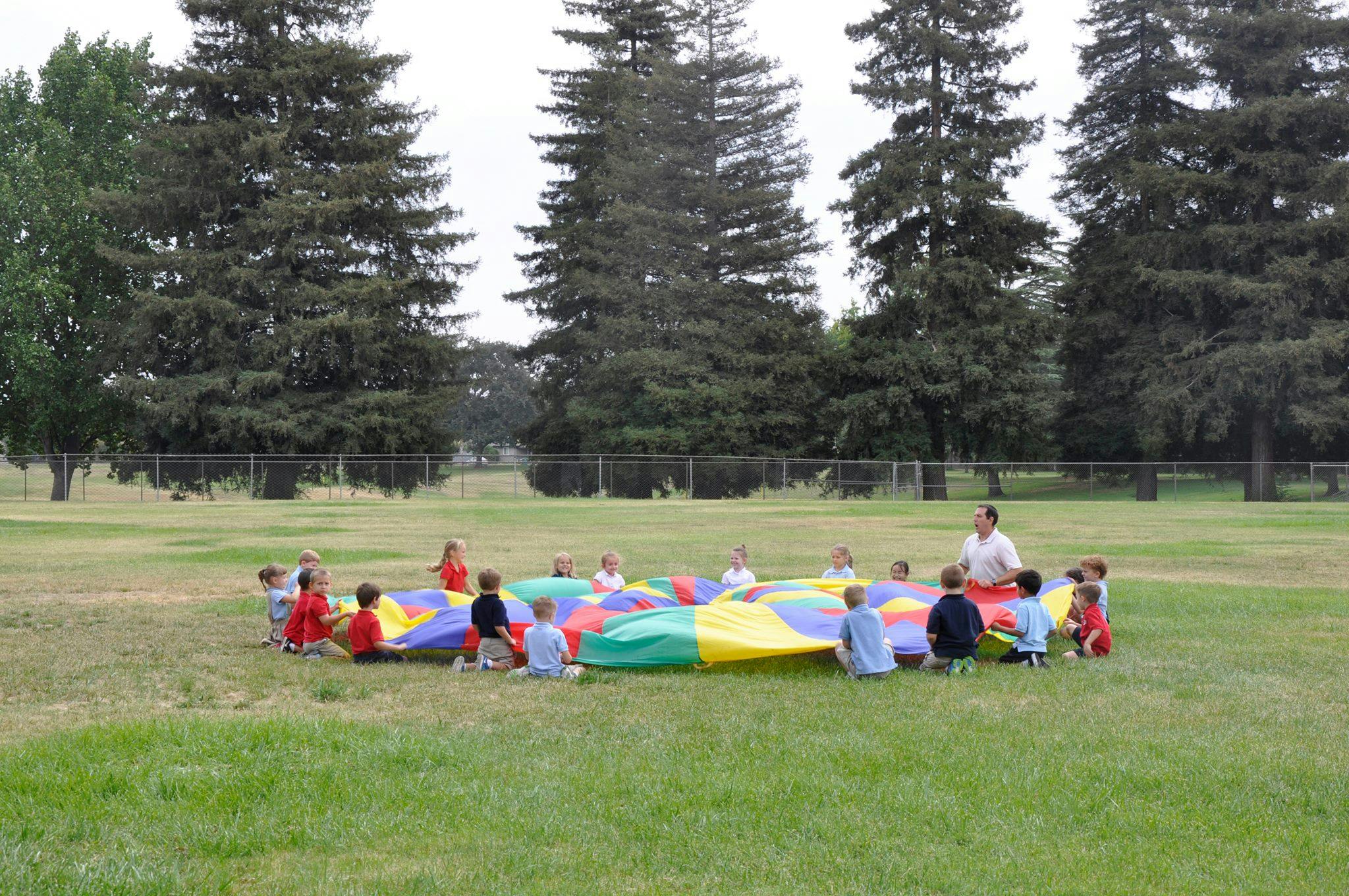Children and an adult playing with a colorful parachute on a grassy field