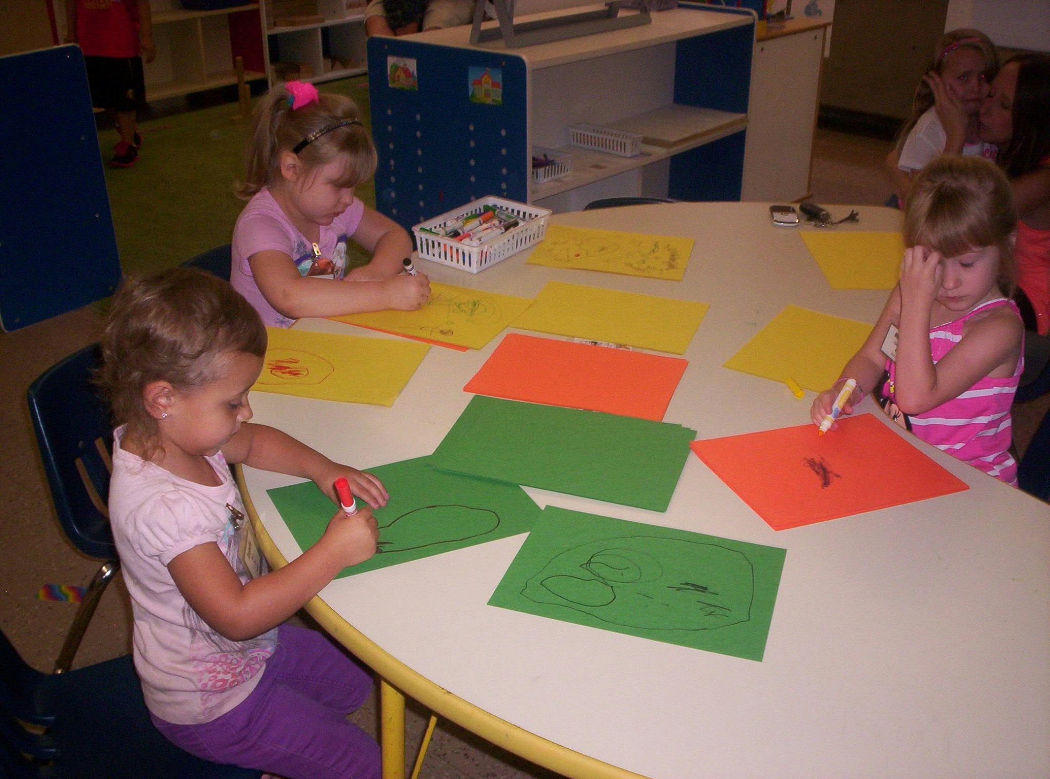 Three children drawing on paper at a table