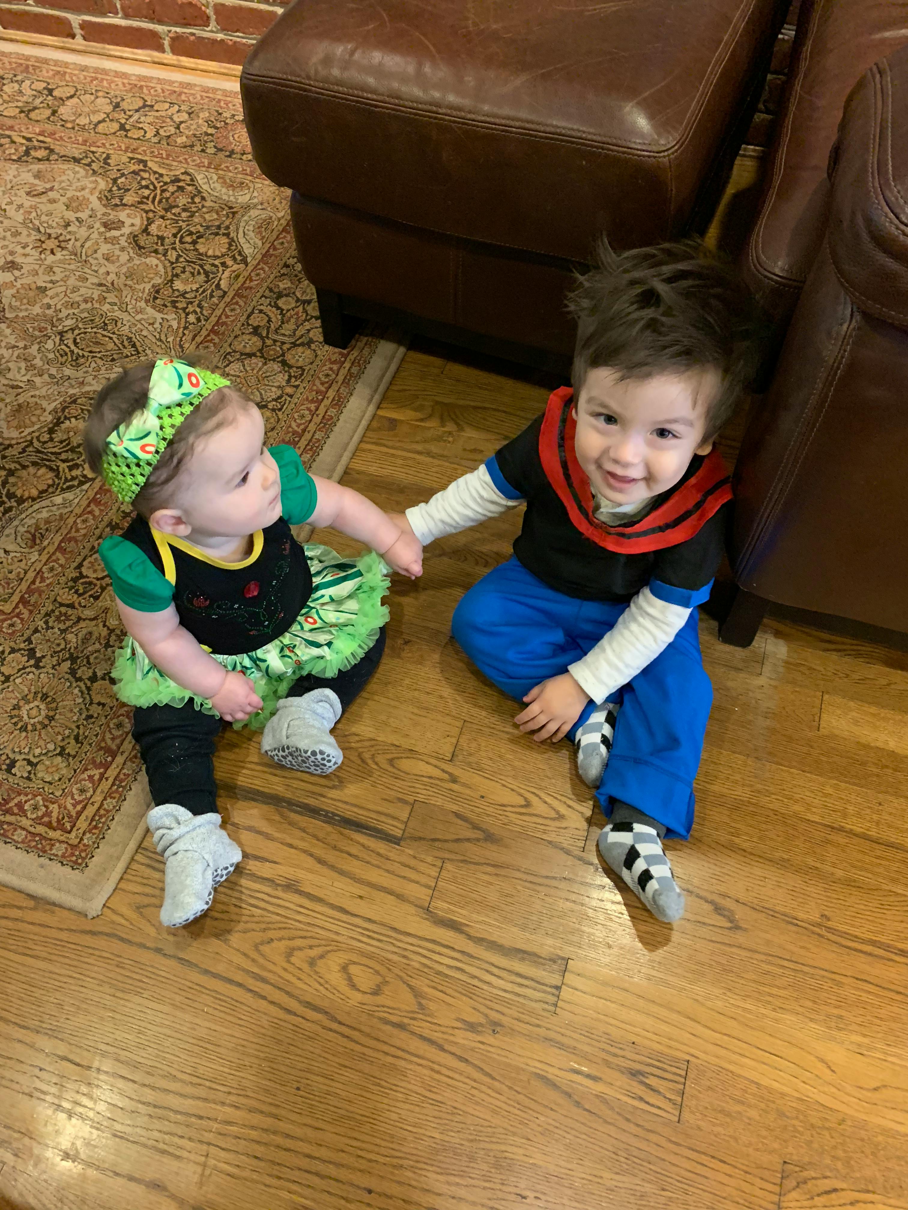 Two children sitting on a wooden floor, holding hands