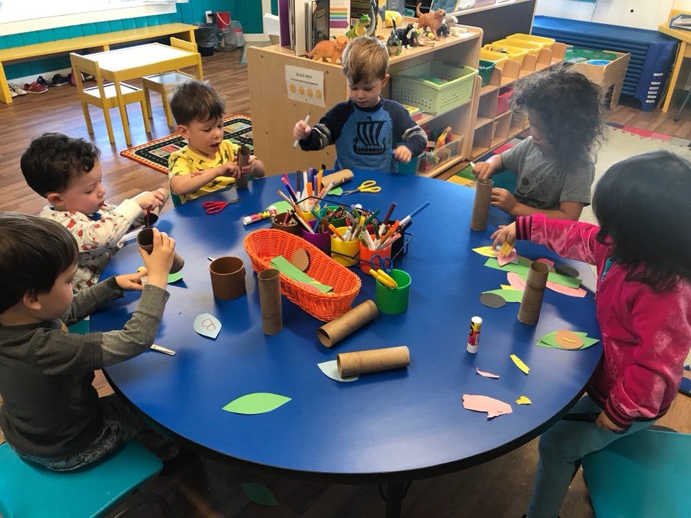 Children doing crafts at a blue table in a classroom