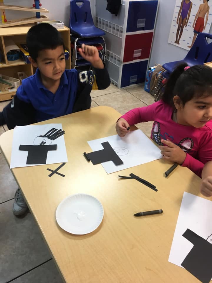 Two children at a table doing crafts with paper cutouts
