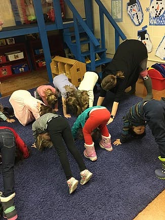 Children and adults bending over in a classroom