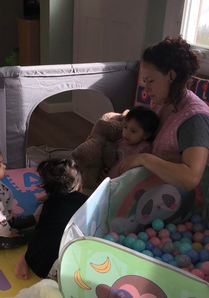 Person with two children and a teddy bear near a ball pit