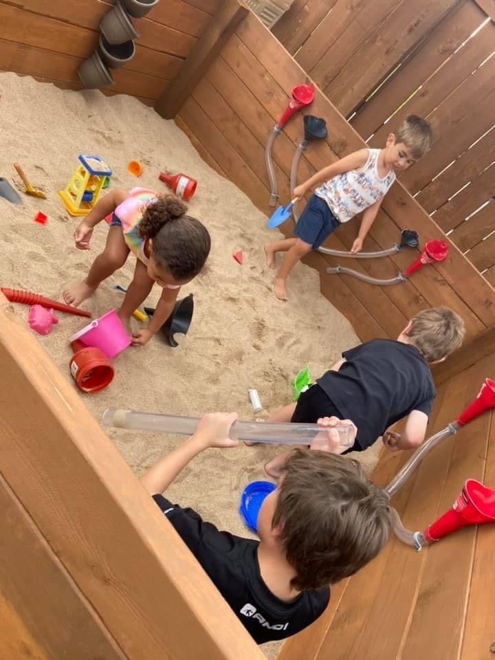Three children playing in a sandbox with toys