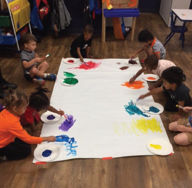 Children painting on a large white sheet on the floor