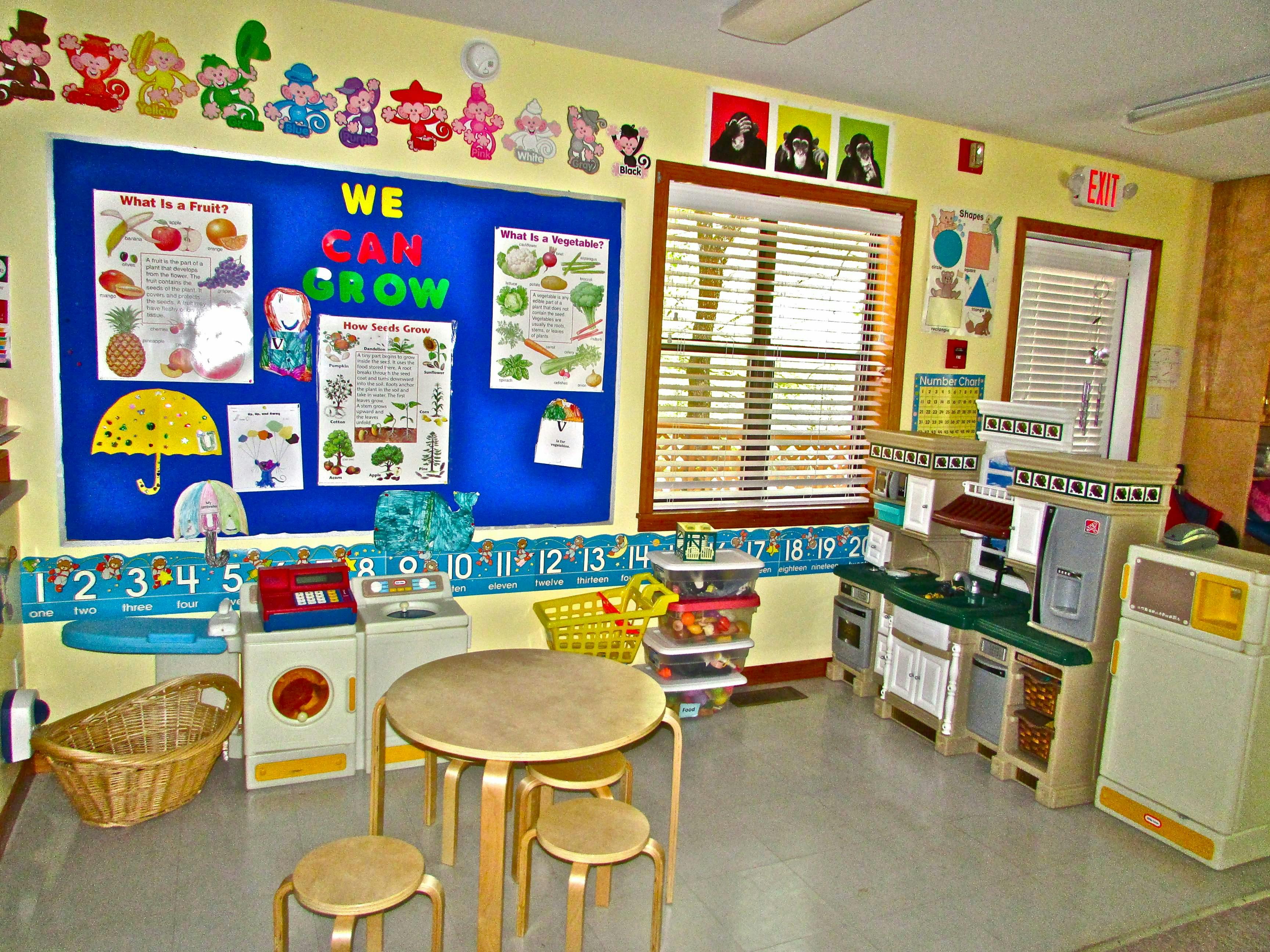 Classroom with bulletin board, play kitchen, and small table with stools