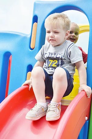 Child sitting on a red slide with another child behind