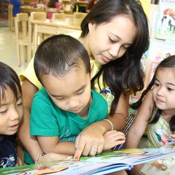 Adult and three children looking at a book in a classroom