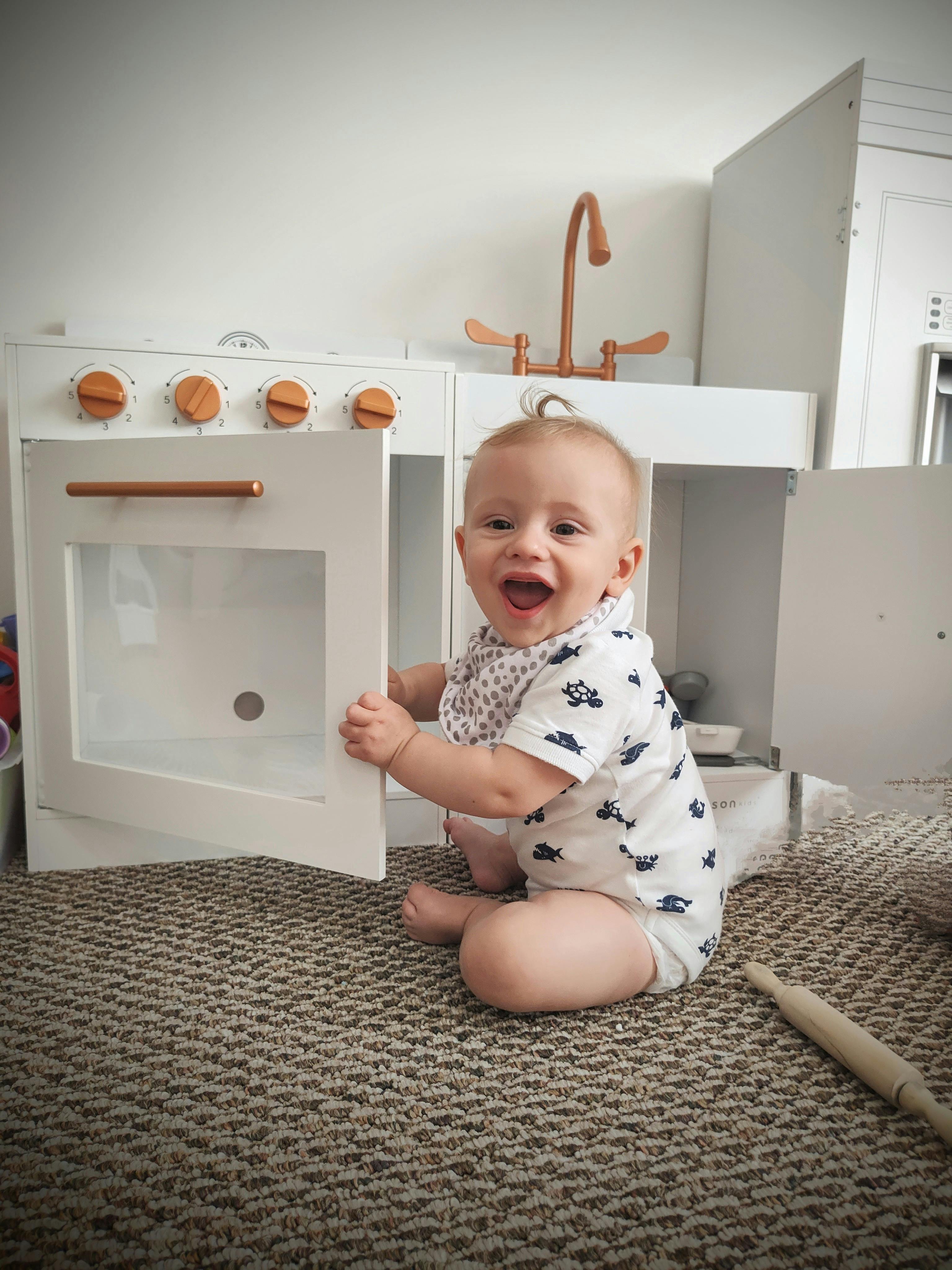 Child sitting on floor opening a toy oven door
