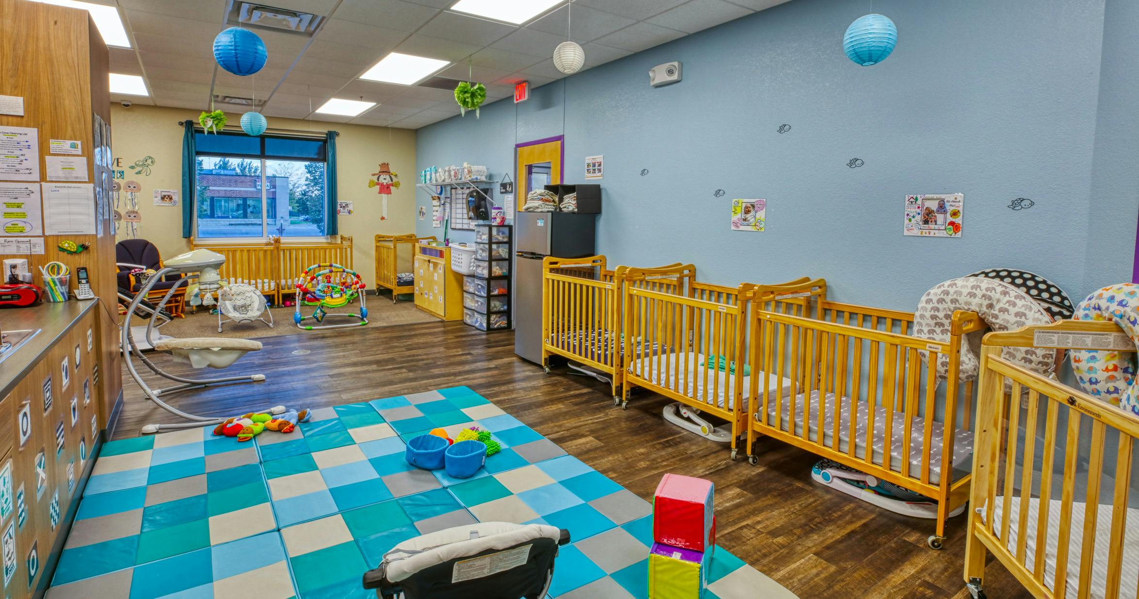 A childcare classroom with cribs, play mats, and infant swings