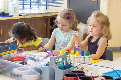 Three children drawing and painting at a table in a classroom