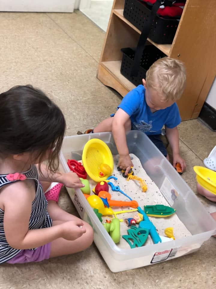 Two children playing with toys in a sand bin