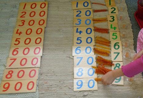 Child's hand arranging number blocks and beads for counting