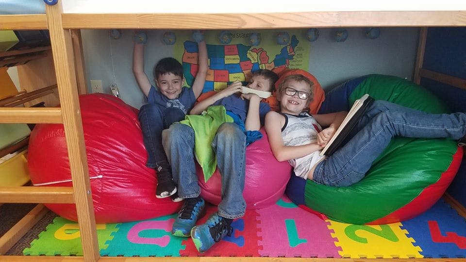 Three children sitting on beanbag chairs under a bunk bed