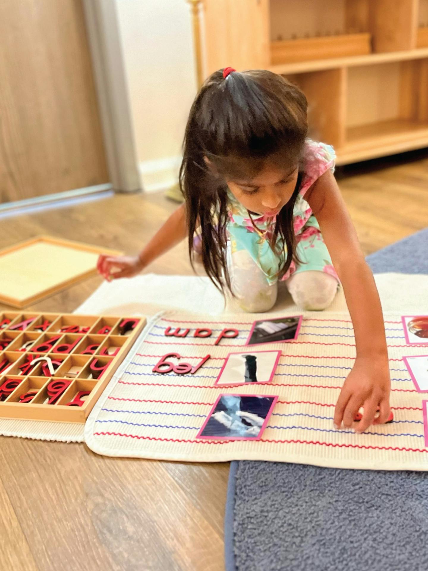 Child kneeling on floor, arranging letter tiles and picture cards