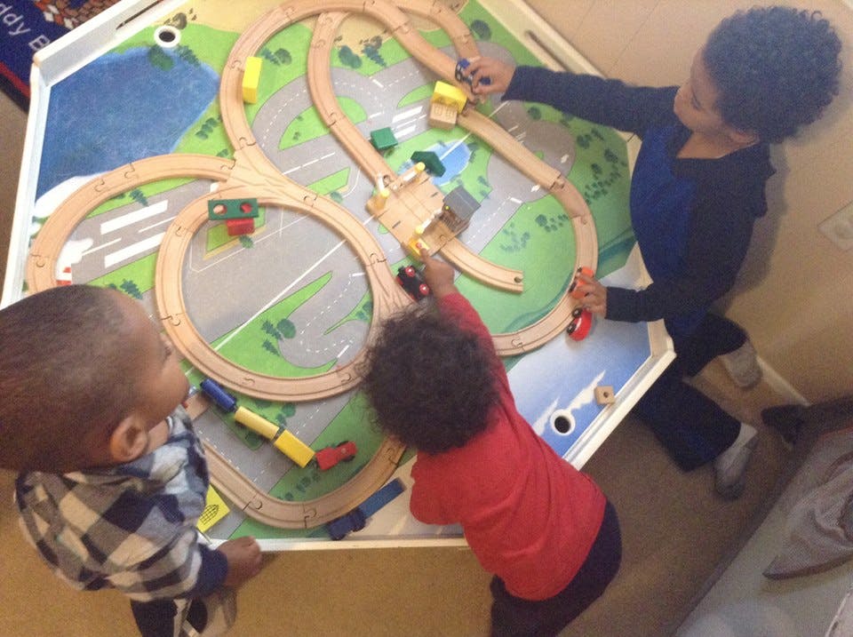 Three children playing with a wooden train set on a table