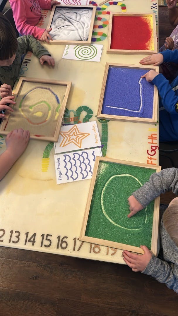 Children tracing shapes in colorful sand trays