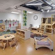 Classroom with small tables and chairs, shelves, and wooden play structures