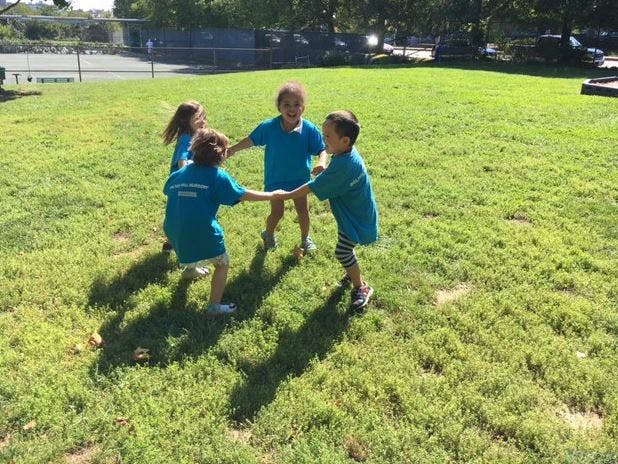 Four children holding hands in a circle on a grassy field