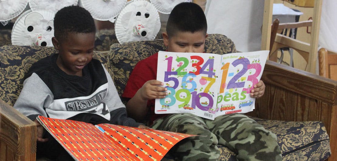 Two children sitting on a couch, one reading a book with numbers