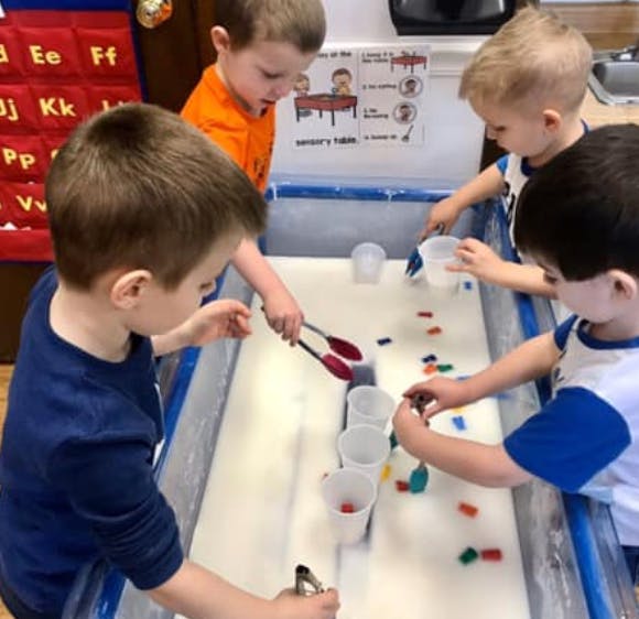 Children playing at a sensory table with cups and small objects