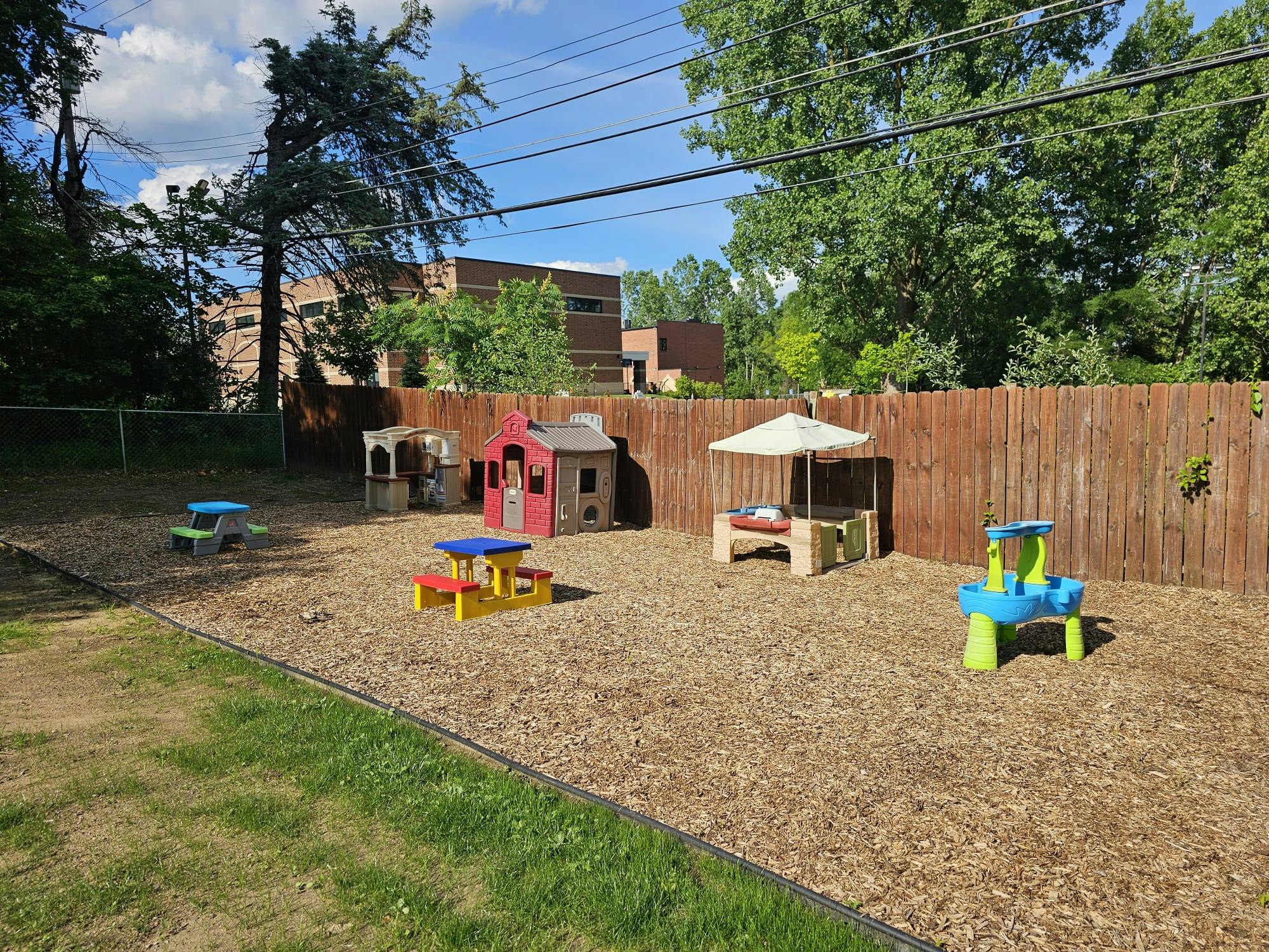 Plastic playhouse and tables in a wood chip playground area