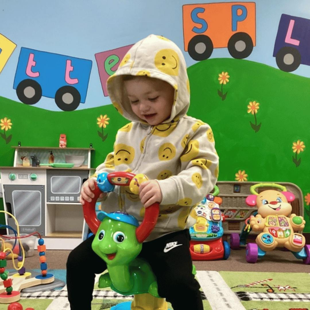 Child on a green turtle ride-on toy in a play area
