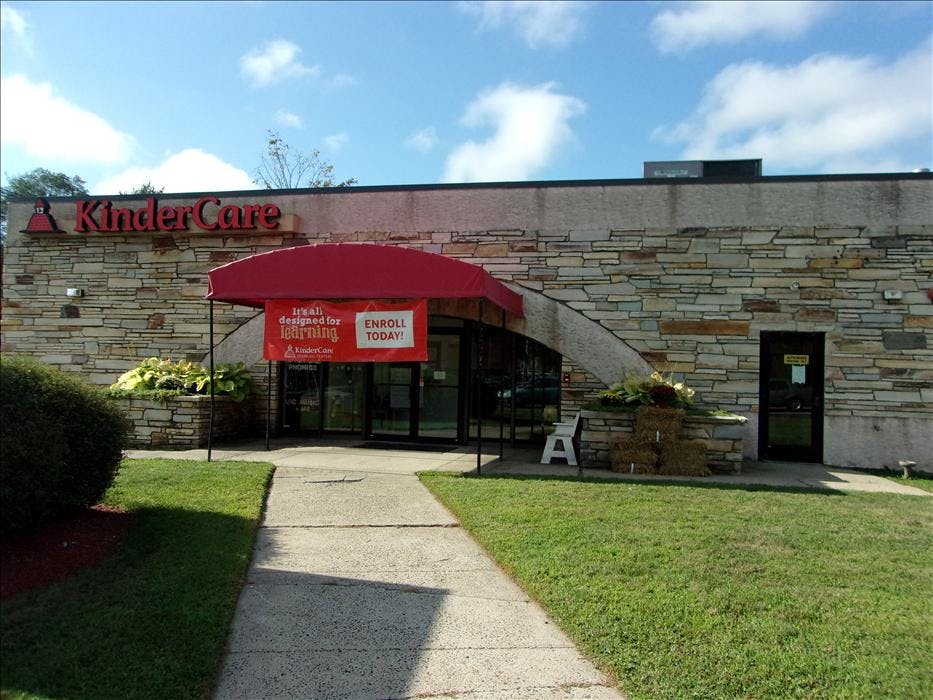 KinderCare building with a red awning and "Enroll Today!" banner