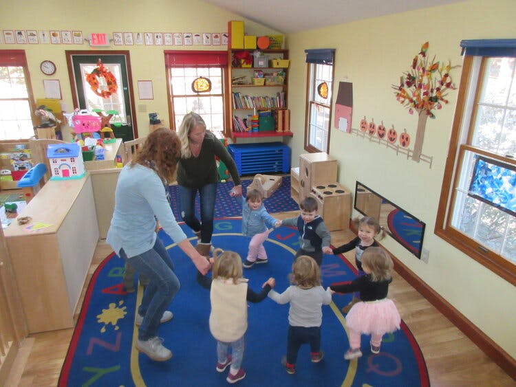 Two people and several children holding hands in a circle in a classroom