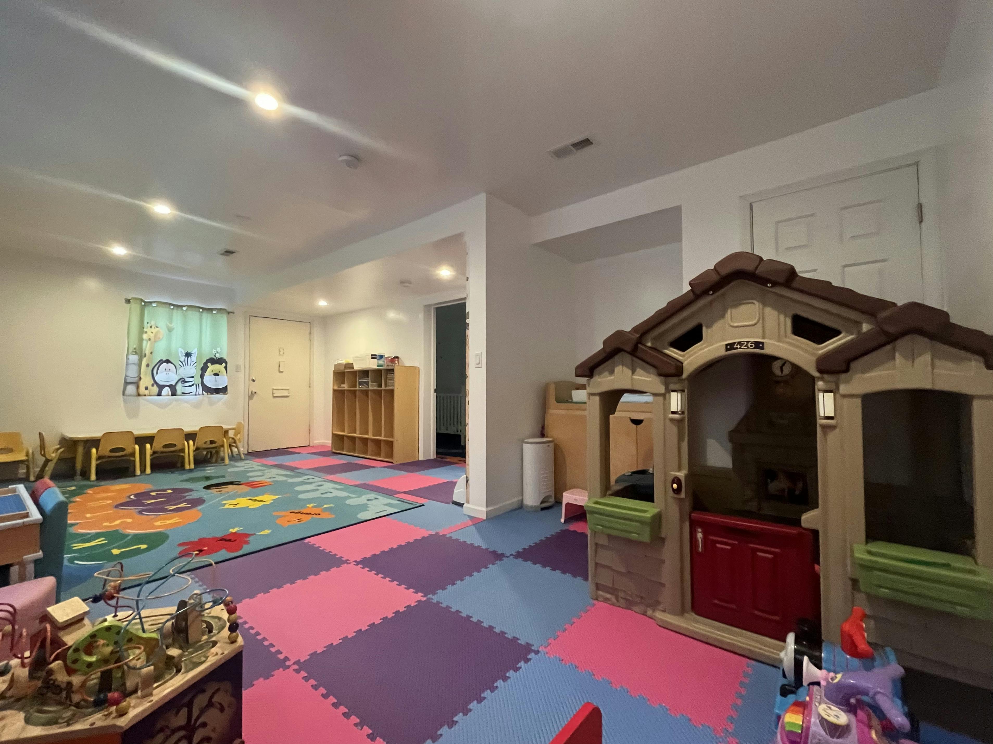 Playroom with a small playhouse, children's tables, and colorful floor mats