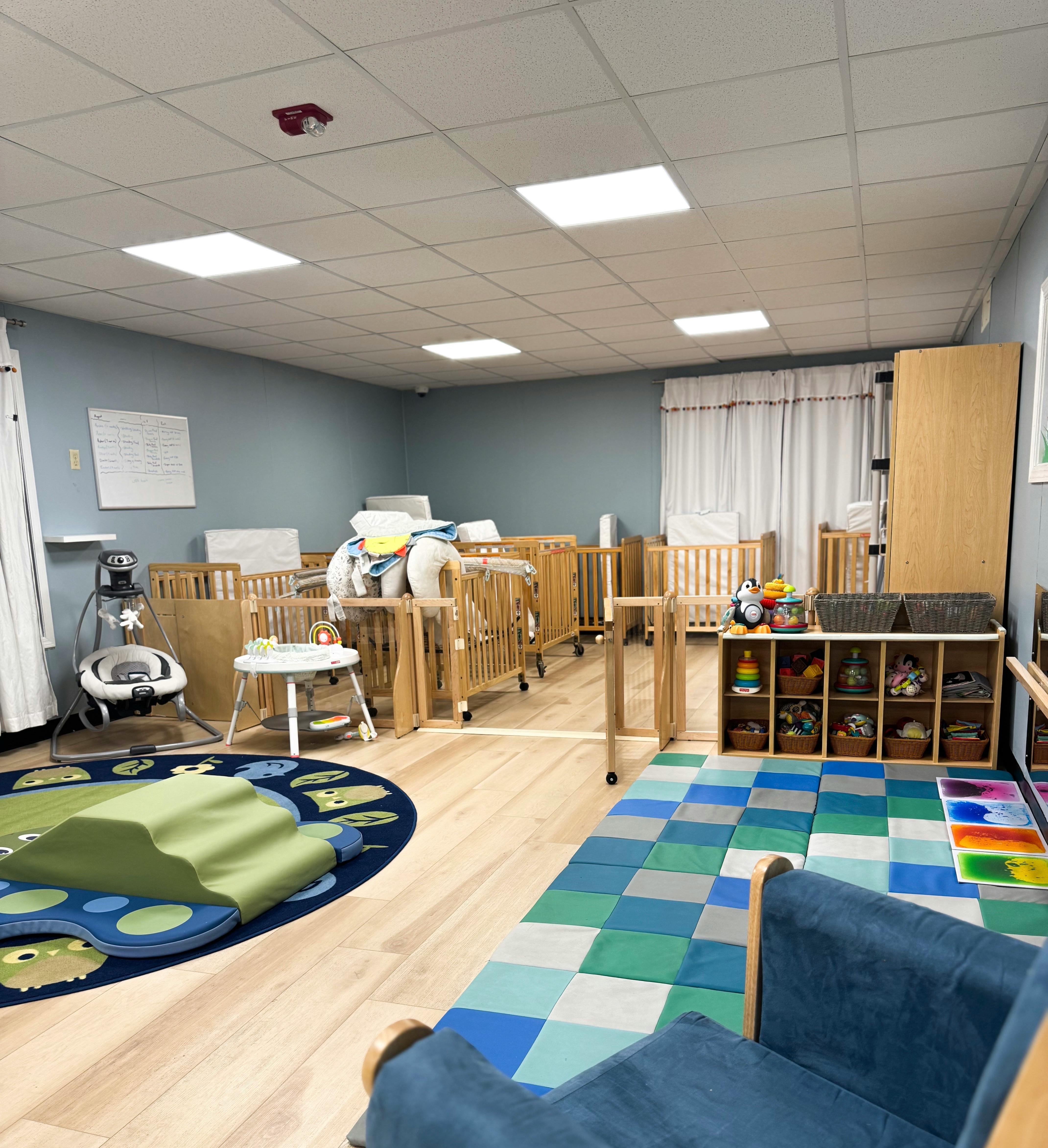 Nursery room with multiple cribs, play mats, and storage shelves
