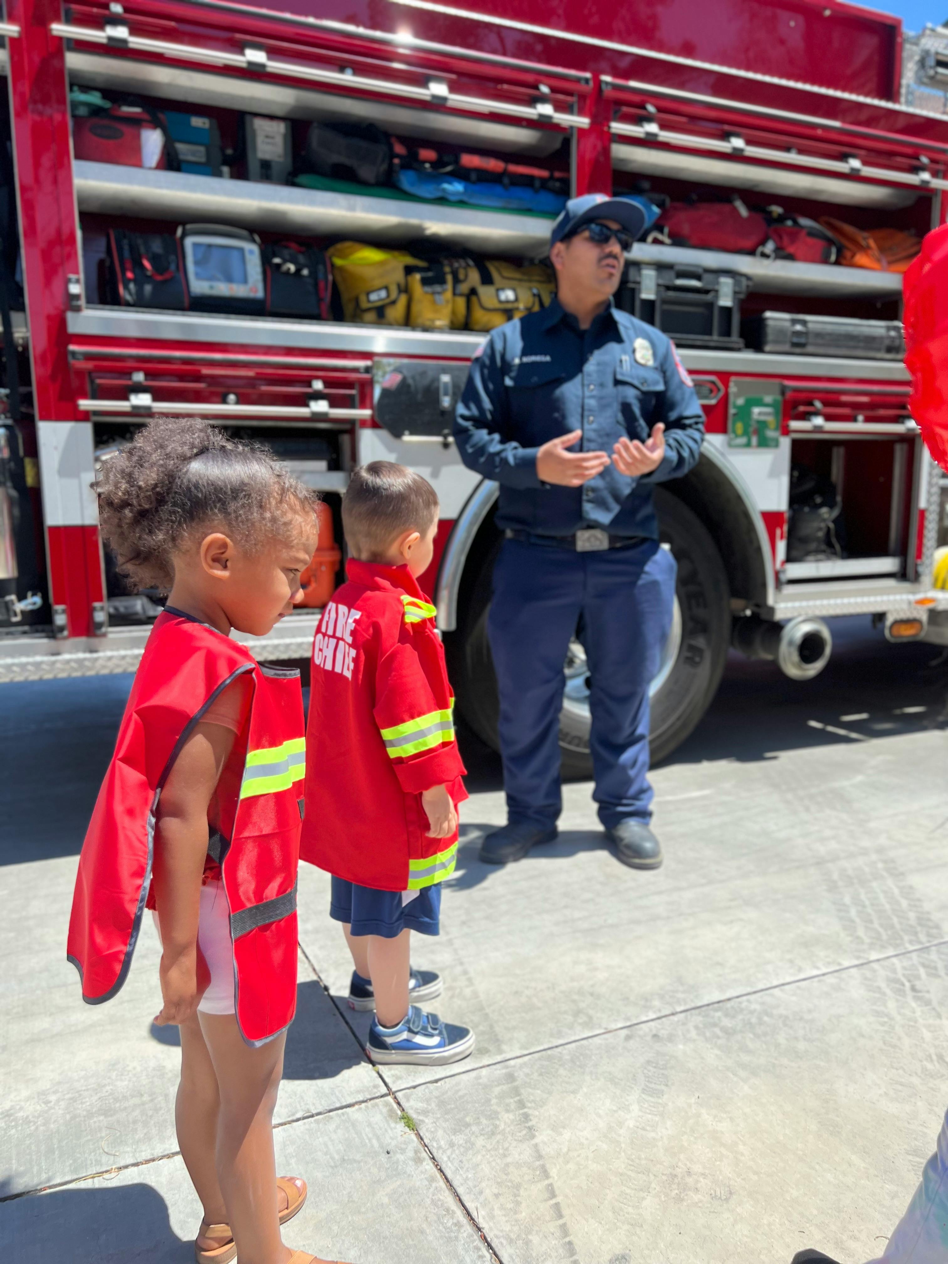 Firefighter speaking to two children in front of a fire truck