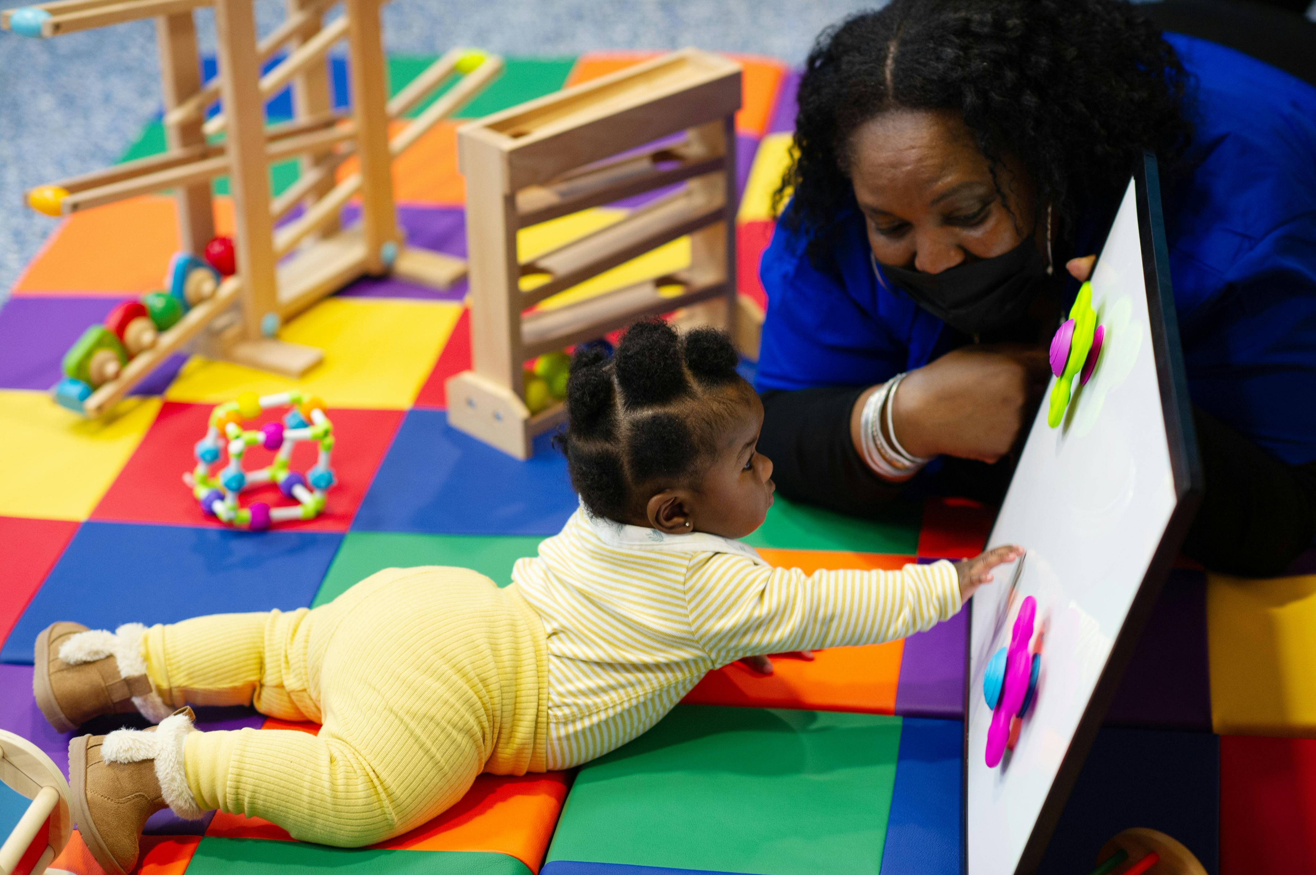 Adult and child playing with a toy on a colorful mat