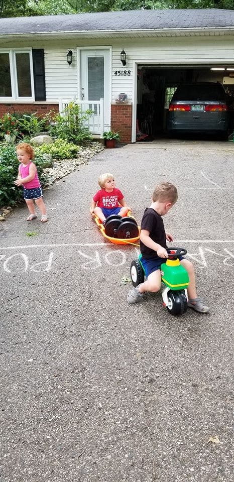 Child on a ride-on toy pulling another child in a wagon, with a third child standing