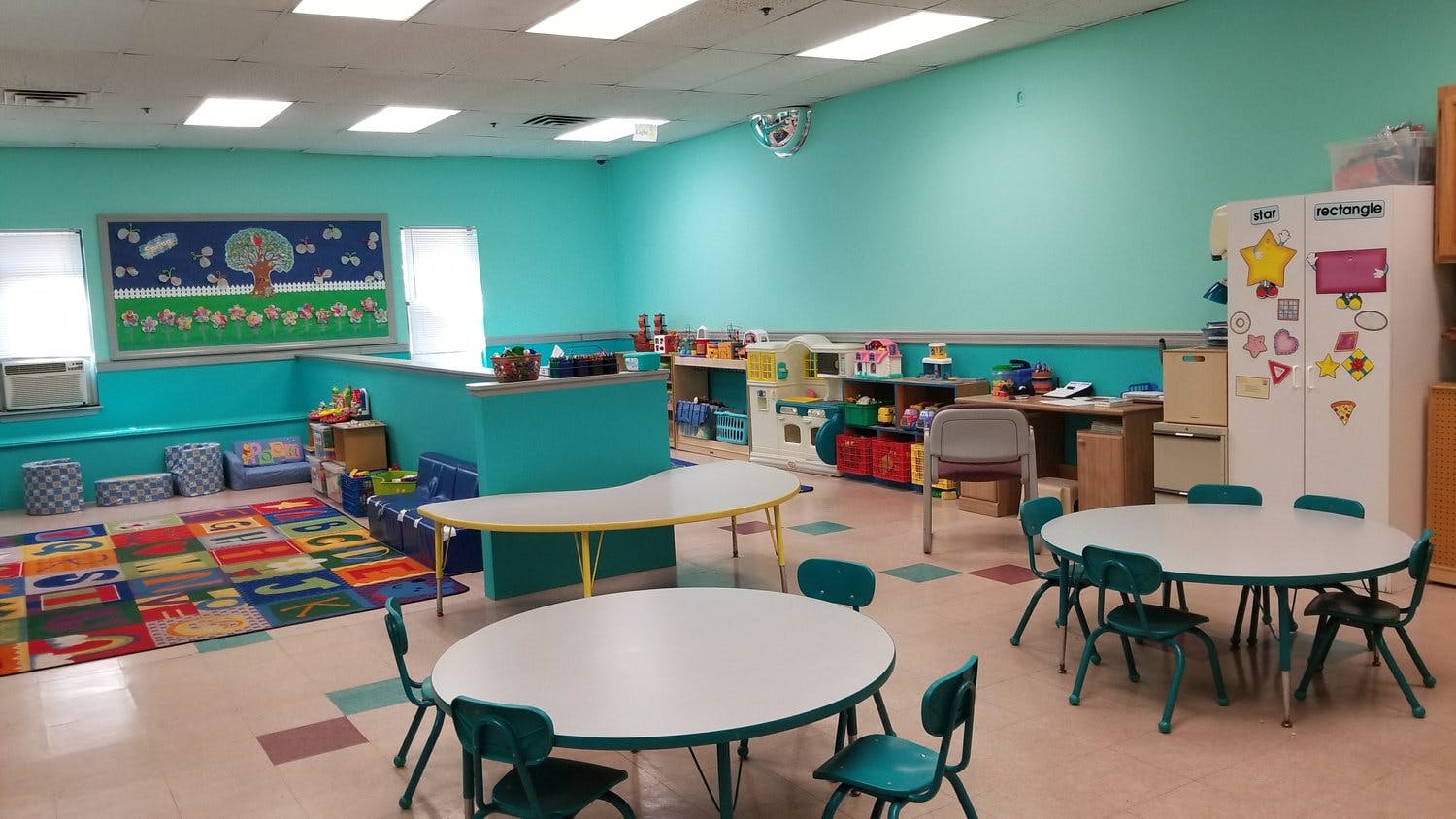 Classroom with small tables and chairs, colorful rug, and light blue walls