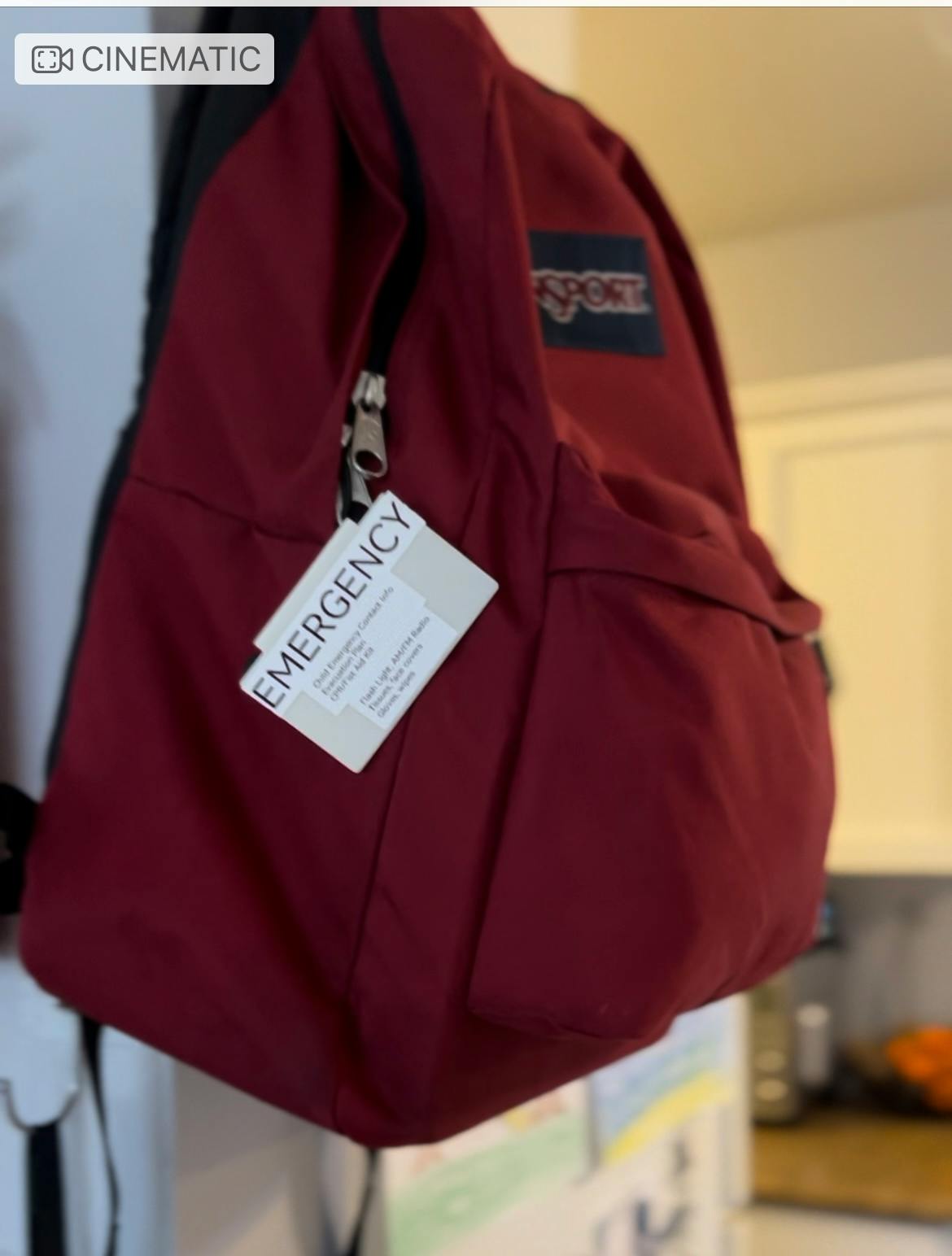Red backpack with an emergency tag attached to the zipper