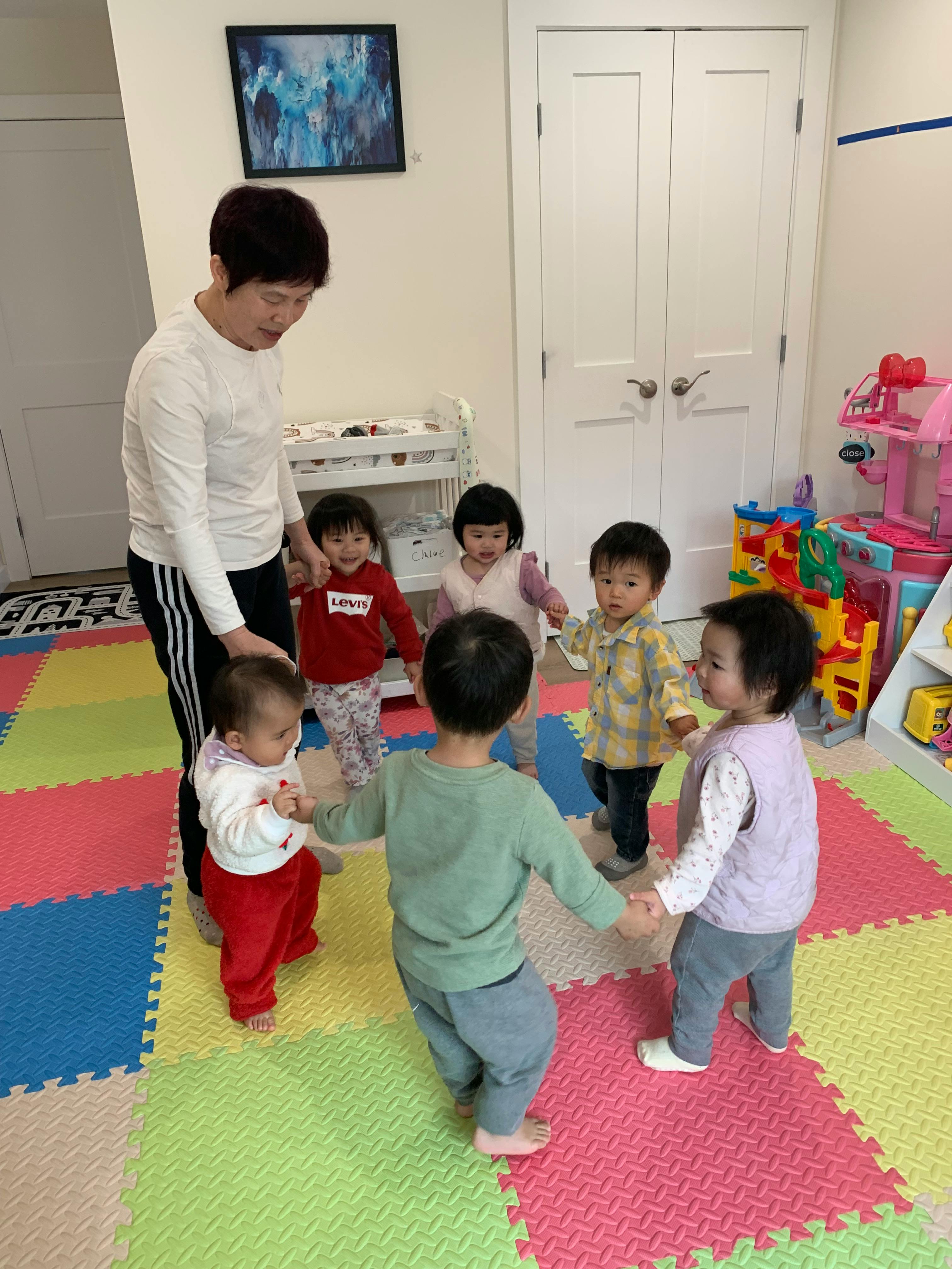 Group of children holding hands in a circle with an adult in a play area