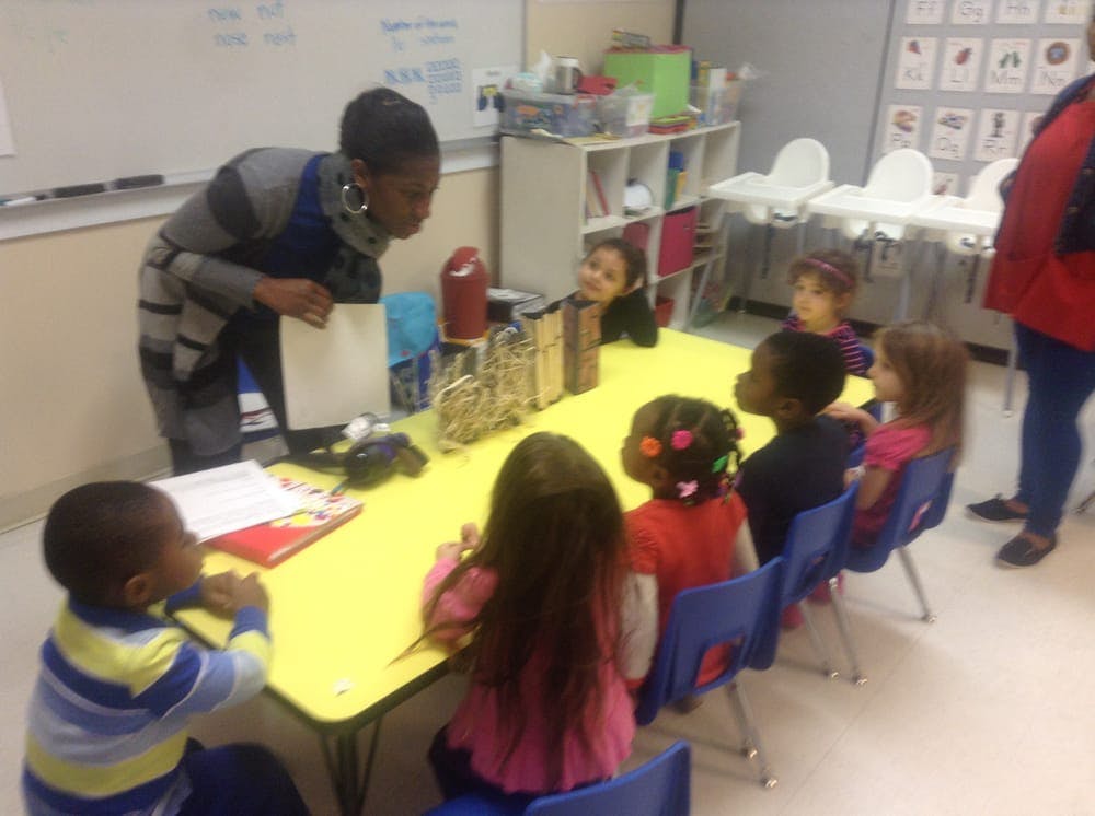 Person standing over a table with several children seated around it in a classroom