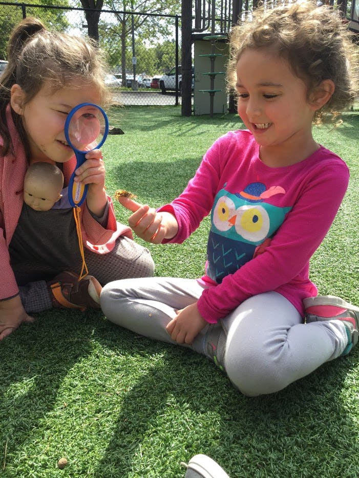 Two children on grass, one holding a magnifying glass, the other holding a small object