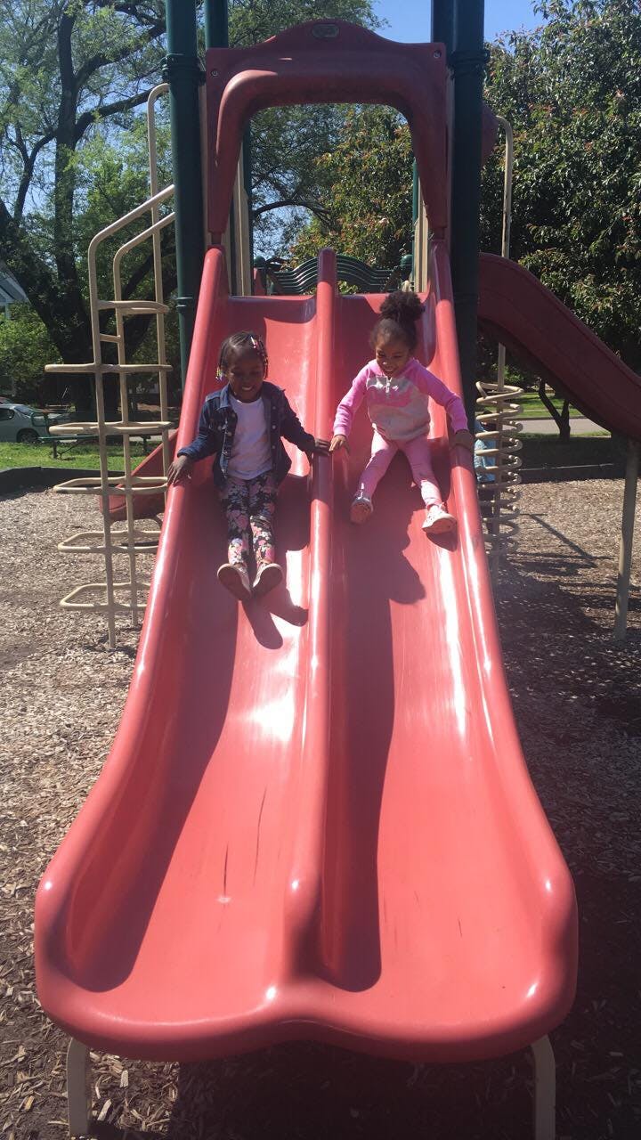 Two children sliding down a red playground slide