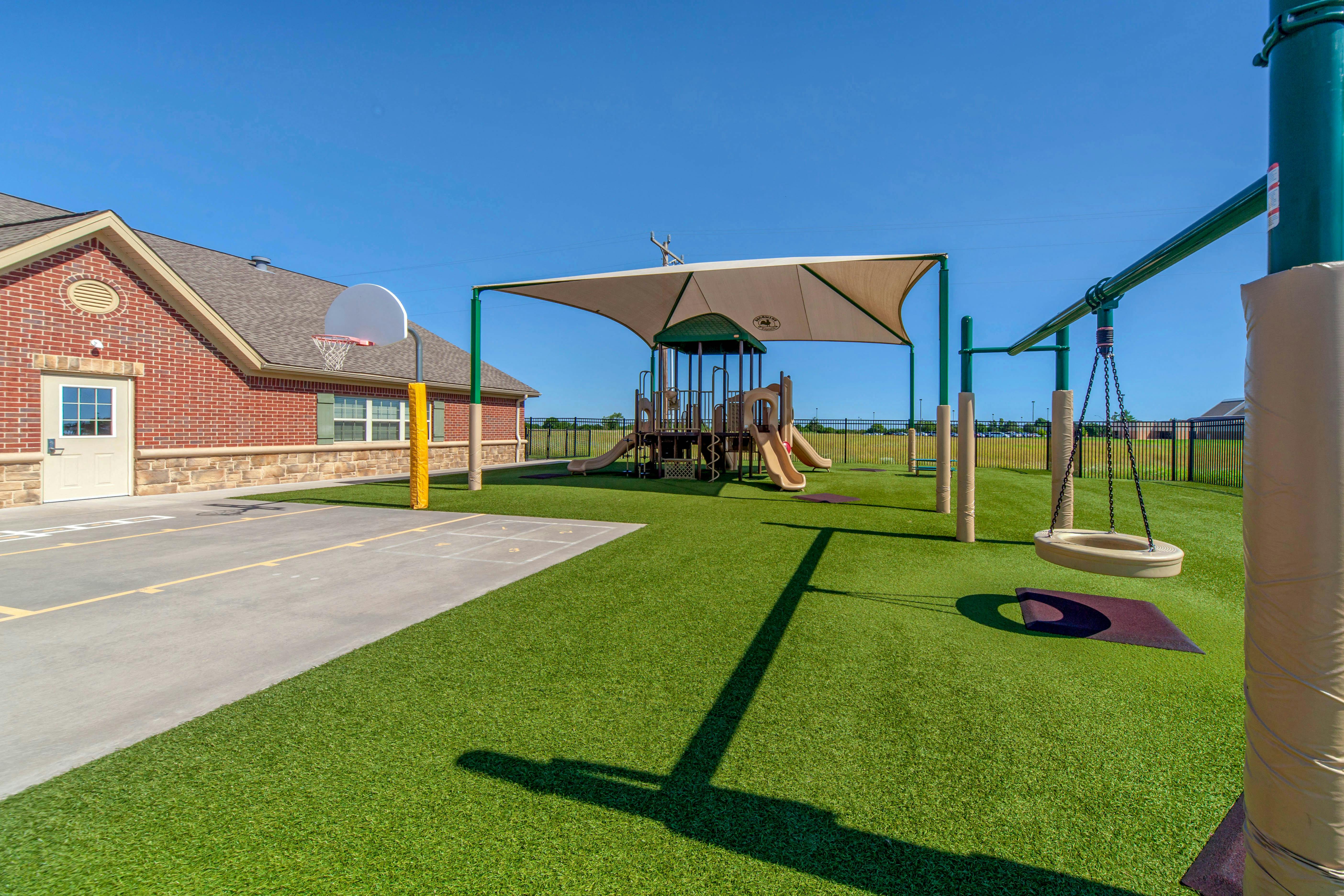 Outdoor playground with artificial turf, slides, swings, and a basketball hoop