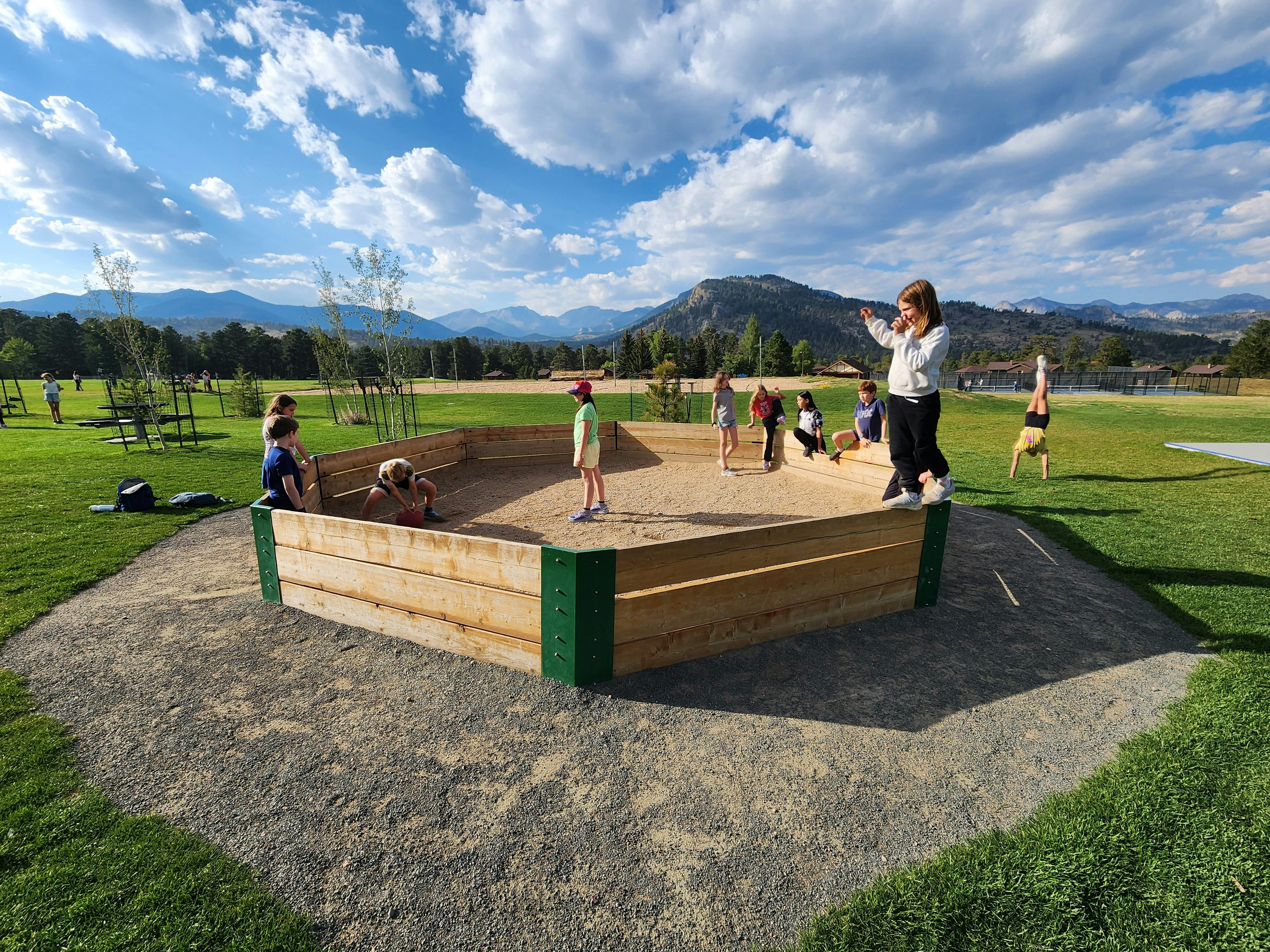 Children playing in a large sandbox with mountains in the background