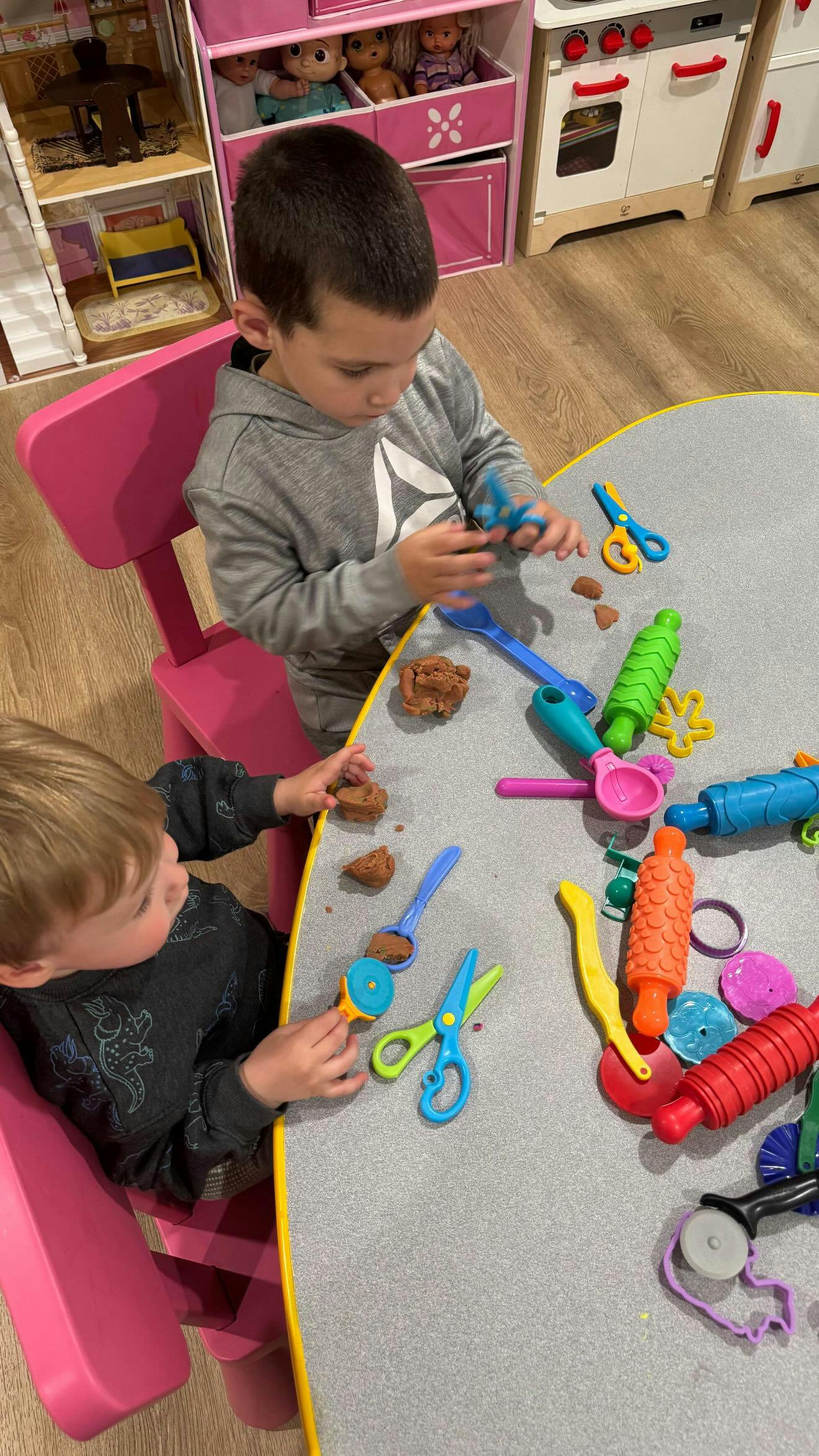 Two children sitting at a table playing with modeling clay and plastic tools