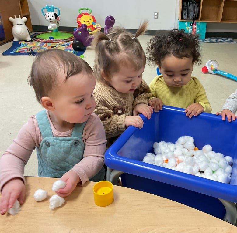 Three children playing with cotton balls in a blue bin
