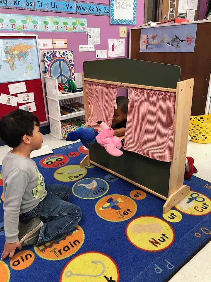 Child watching another child use puppets in a puppet theater