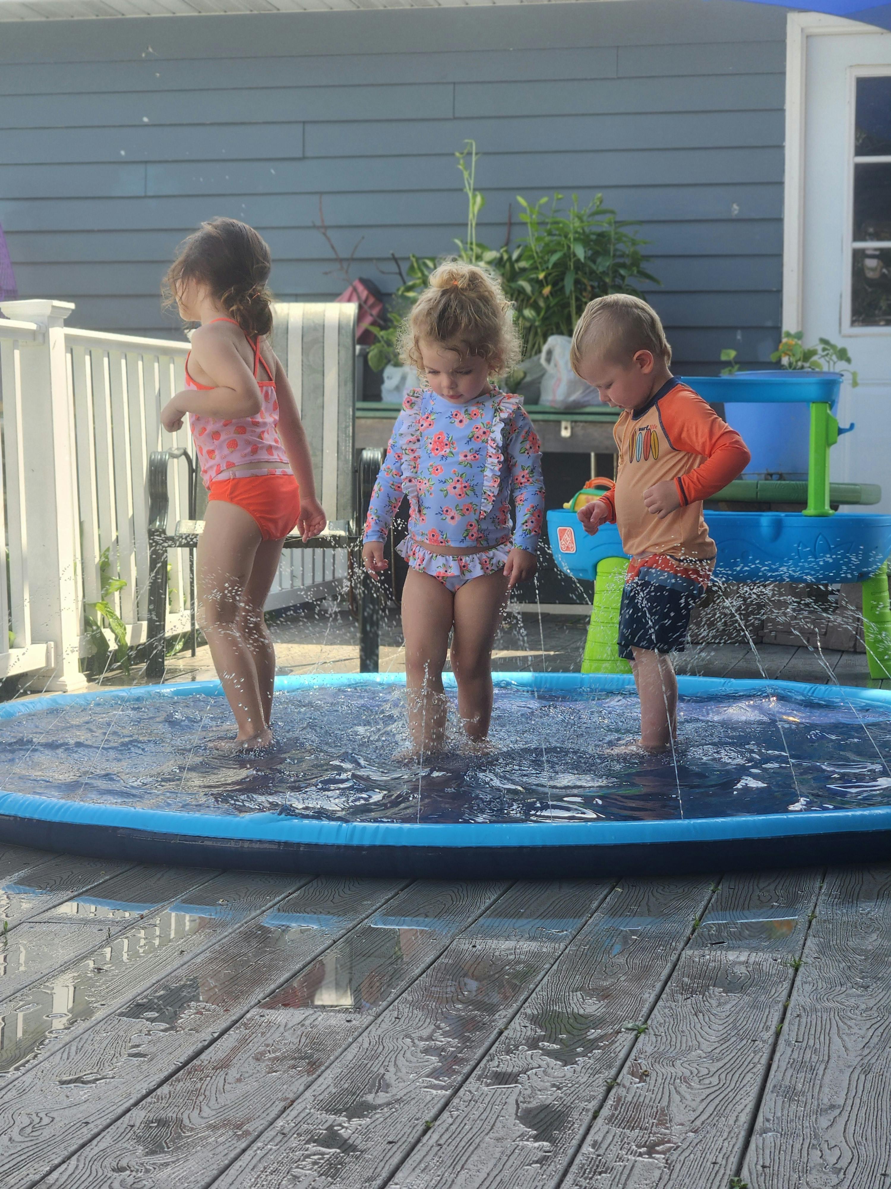 Three children playing in a small inflatable pool on a deck