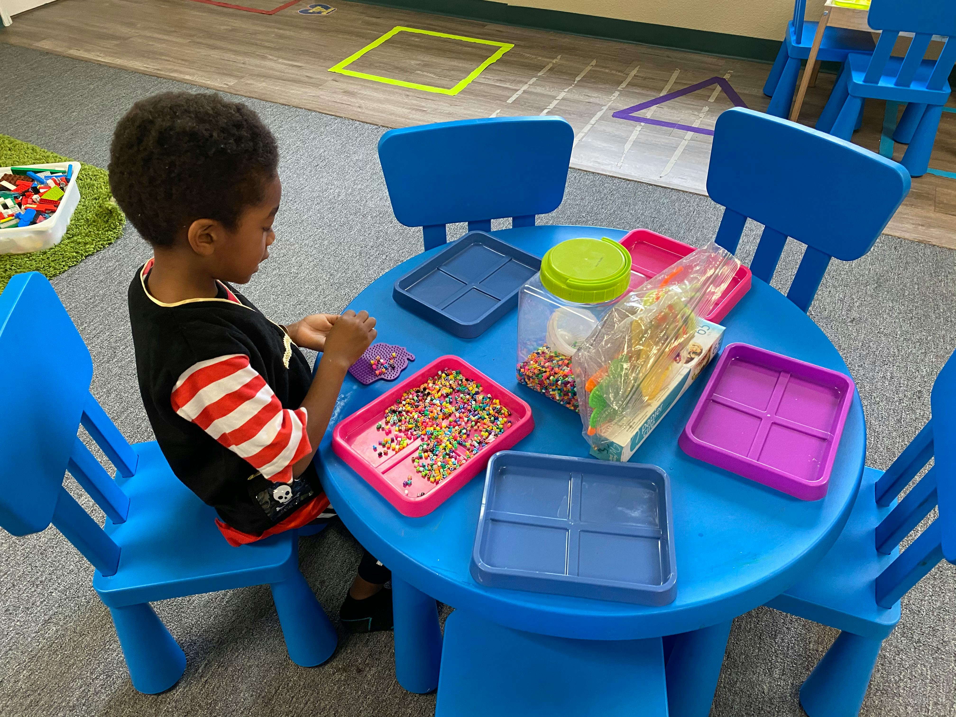 Child sitting at a blue table with colorful sprinkles and trays